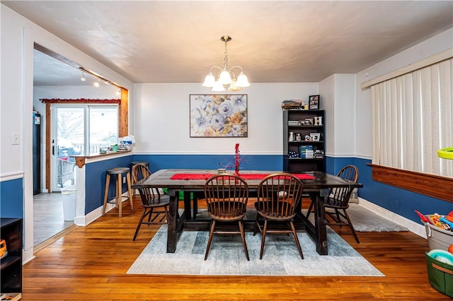 dining room with rail lighting, wood-type flooring, and a chandelier