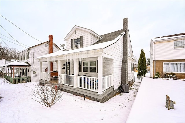 snow covered rear of property featuring a porch and central air condition unit