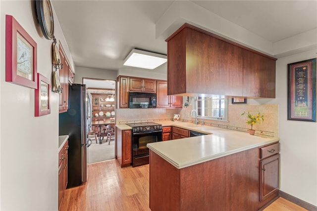 kitchen featuring black appliances, light hardwood / wood-style flooring, sink, and kitchen peninsula