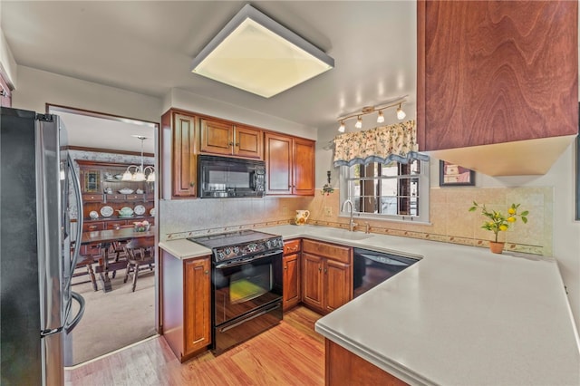 kitchen with pendant lighting, black appliances, decorative backsplash, light wood-type flooring, and sink