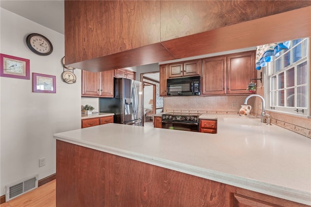 kitchen with black appliances, light hardwood / wood-style floors, kitchen peninsula, sink, and backsplash