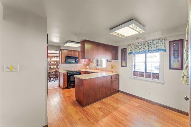 kitchen featuring black appliances, kitchen peninsula, sink, light hardwood / wood-style flooring, and backsplash