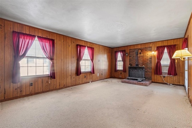 unfurnished living room with a wood stove, light colored carpet, and wooden walls