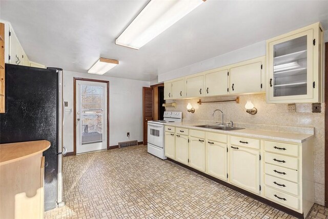 kitchen featuring cream cabinetry, decorative backsplash, stainless steel refrigerator, white electric range, and sink