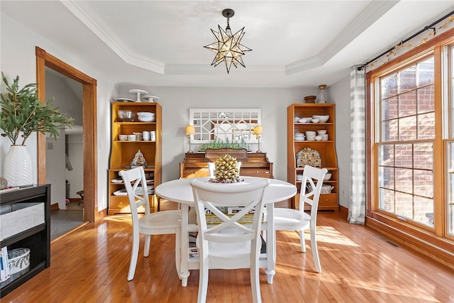 dining area featuring a healthy amount of sunlight, light wood-type flooring, a chandelier, and a tray ceiling