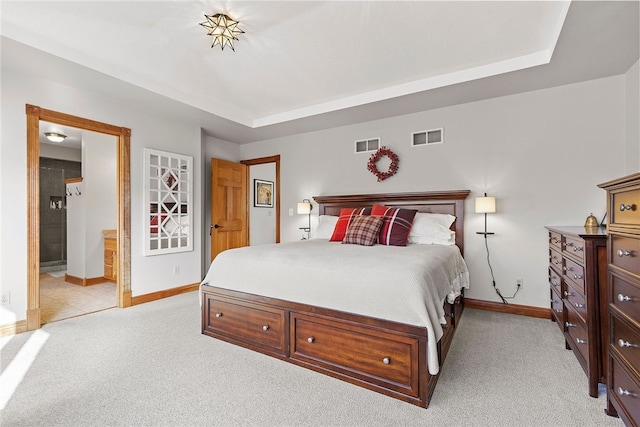 bedroom with ensuite bath, a raised ceiling, and light carpet