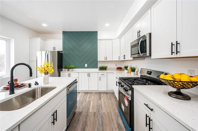 kitchen with light stone countertops, light hardwood / wood-style flooring, white cabinetry, appliances with stainless steel finishes, and sink