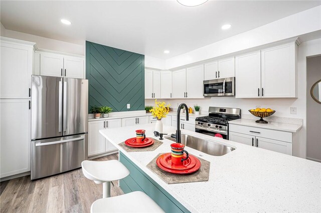 kitchen featuring light stone countertops, stainless steel appliances, white cabinets, a kitchen breakfast bar, and sink