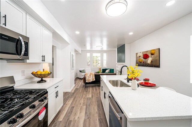 kitchen with stainless steel appliances, a kitchen island with sink, light hardwood / wood-style floors, and white cabinets