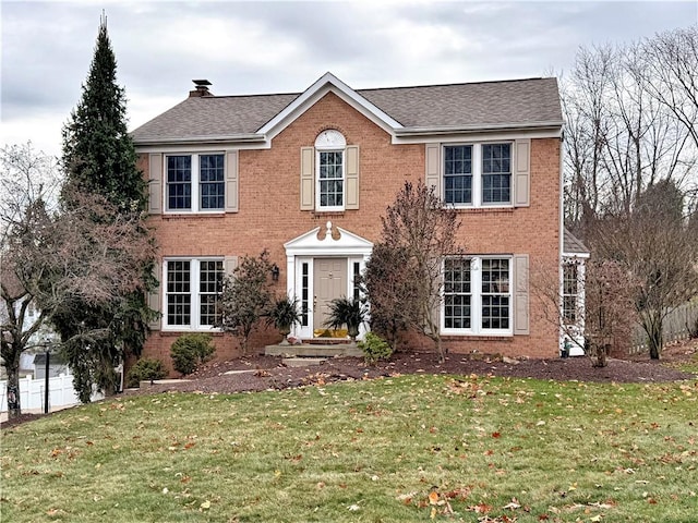 colonial home featuring brick siding, a chimney, a front lawn, and a shingled roof