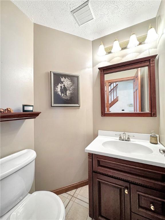 bathroom with toilet, a textured ceiling, tile patterned floors, and vanity