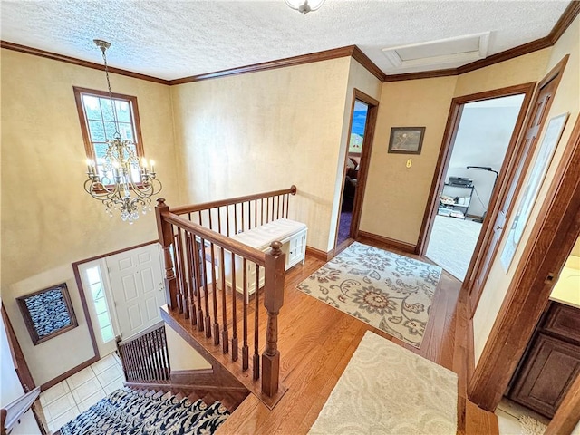 foyer entrance featuring a textured ceiling, light hardwood / wood-style flooring, ornamental molding, and a notable chandelier