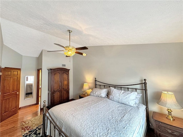 bedroom featuring lofted ceiling, ceiling fan, a textured ceiling, and light hardwood / wood-style floors