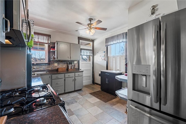 kitchen featuring gas range oven, stainless steel fridge, decorative backsplash, gray cabinetry, and ceiling fan