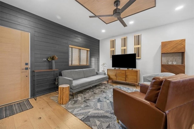 living room with wood walls, ceiling fan, and light hardwood / wood-style floors