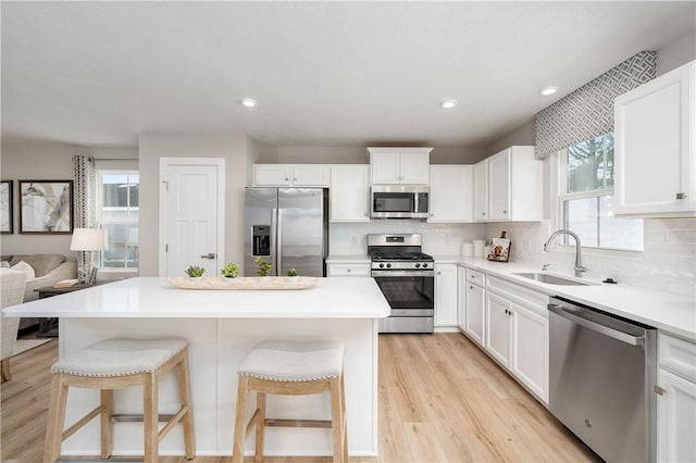 kitchen featuring white cabinets, stainless steel appliances, a breakfast bar, a kitchen island, and sink