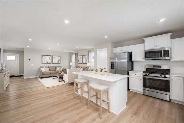 kitchen with white cabinetry, light hardwood / wood-style floors, a breakfast bar area, a kitchen island, and appliances with stainless steel finishes