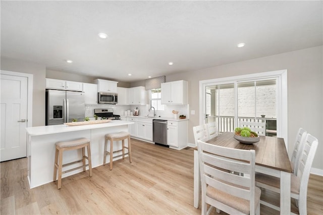 kitchen with appliances with stainless steel finishes, light hardwood / wood-style floors, a kitchen island, sink, and white cabinetry