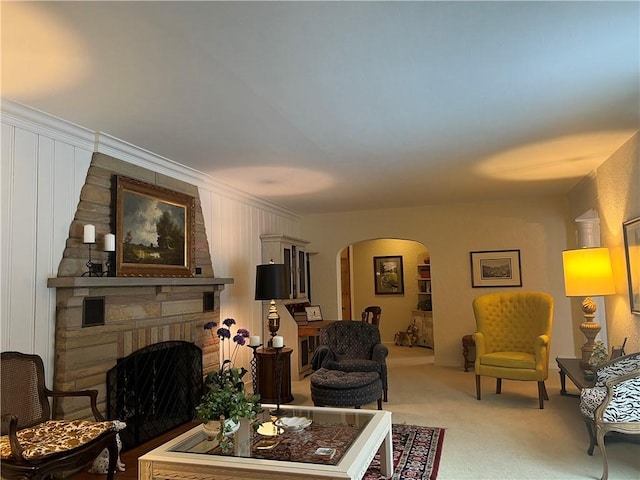 living room with carpet floors, crown molding, and a stone fireplace