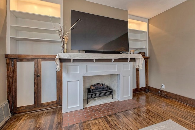 unfurnished living room with a fireplace, built in shelves, and dark hardwood / wood-style floors