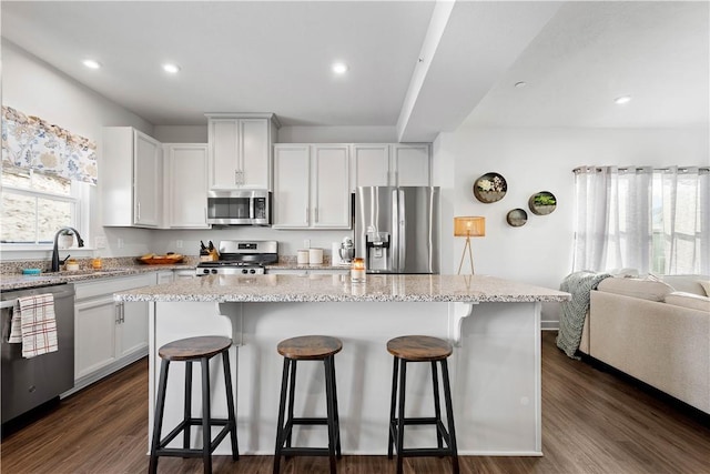 kitchen with stainless steel appliances, a kitchen island, white cabinetry, and light stone counters