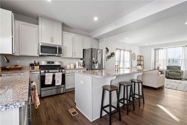 kitchen featuring stainless steel appliances, sink, a kitchen bar, a kitchen island, and dark hardwood / wood-style flooring