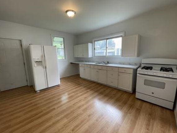 kitchen with white appliances, sink, light wood-type flooring, and white cabinetry