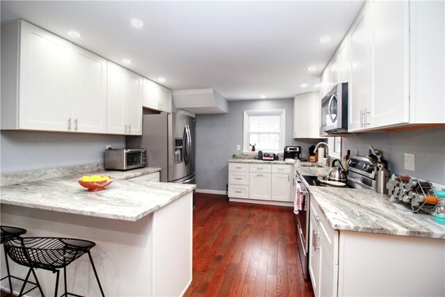 kitchen with kitchen peninsula, a breakfast bar, dark hardwood / wood-style flooring, white cabinetry, and appliances with stainless steel finishes