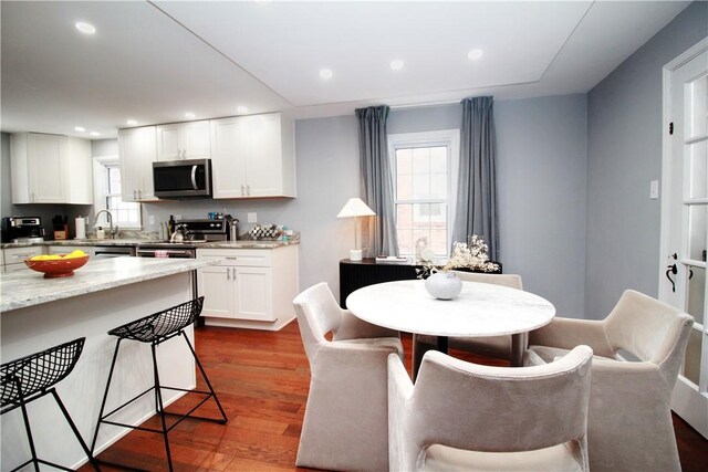 kitchen with stainless steel appliances, white cabinetry, light stone counters, a kitchen breakfast bar, and dark wood-type flooring