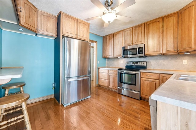 kitchen with light hardwood / wood-style floors, ceiling fan, stainless steel appliances, tasteful backsplash, and a textured ceiling