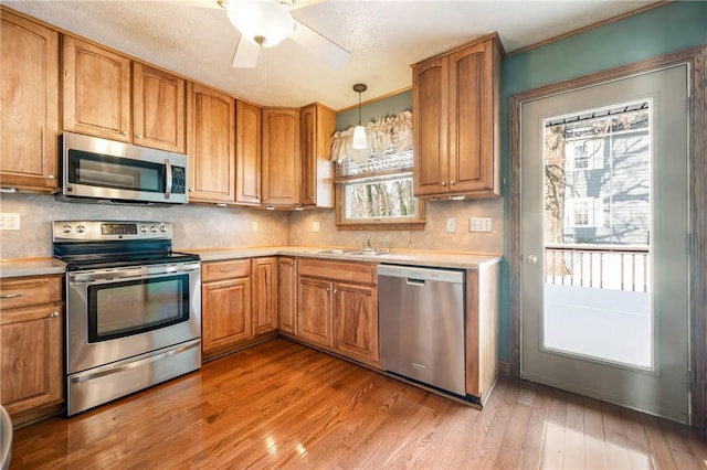 kitchen with decorative light fixtures, stainless steel appliances, light hardwood / wood-style floors, backsplash, and ceiling fan