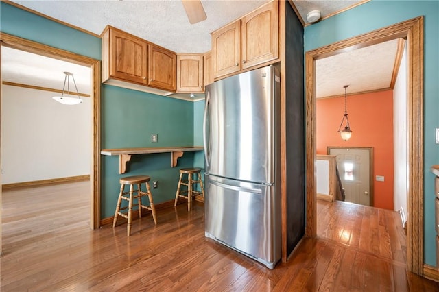 kitchen featuring decorative light fixtures, a textured ceiling, wood-type flooring, and stainless steel refrigerator