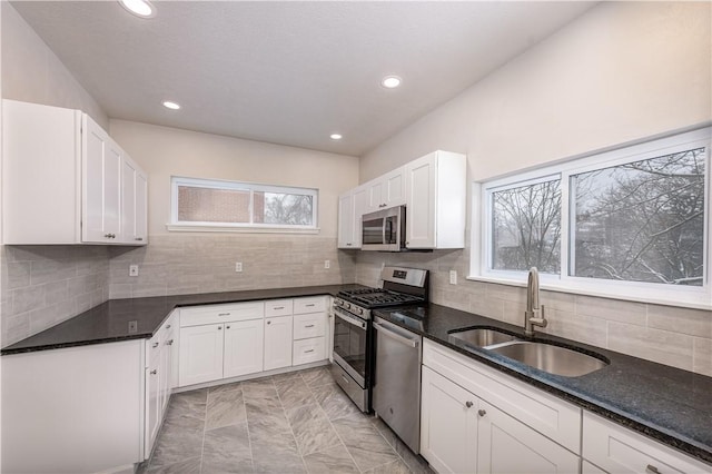 kitchen featuring appliances with stainless steel finishes, dark stone countertops, white cabinets, and sink