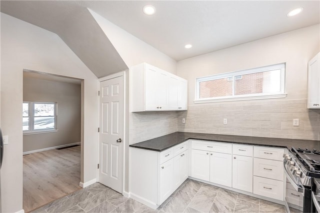 kitchen with vaulted ceiling, backsplash, white cabinets, and stainless steel range with gas stovetop