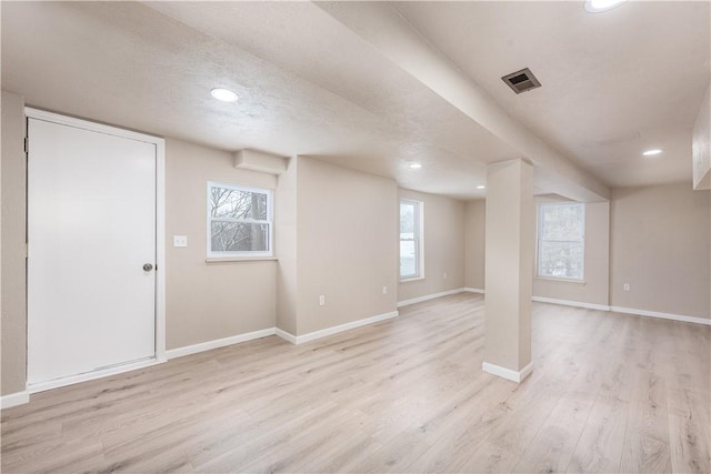 basement with a textured ceiling, a healthy amount of sunlight, and light hardwood / wood-style flooring