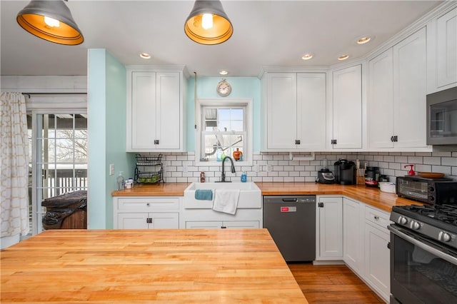 kitchen with appliances with stainless steel finishes, white cabinetry, decorative backsplash, sink, and butcher block countertops