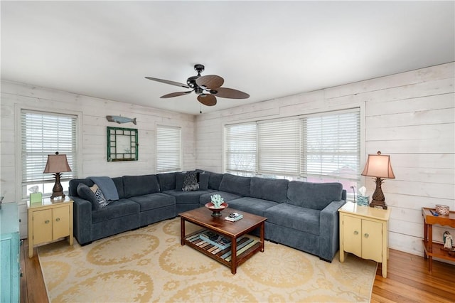 living room with ceiling fan, wooden walls, and light wood-type flooring