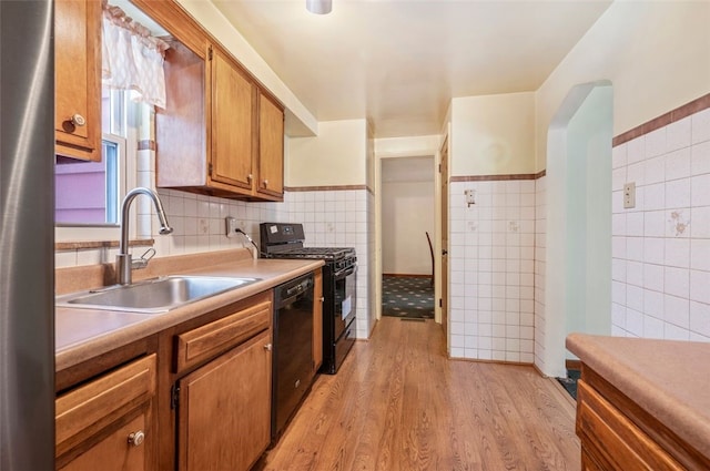 kitchen featuring black appliances, tile walls, sink, and light hardwood / wood-style flooring