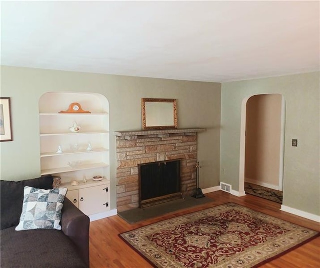 living room featuring built in shelves, wood-type flooring, and a fireplace