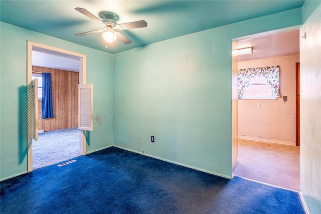 unfurnished room featuring ceiling fan, wood walls, and dark colored carpet