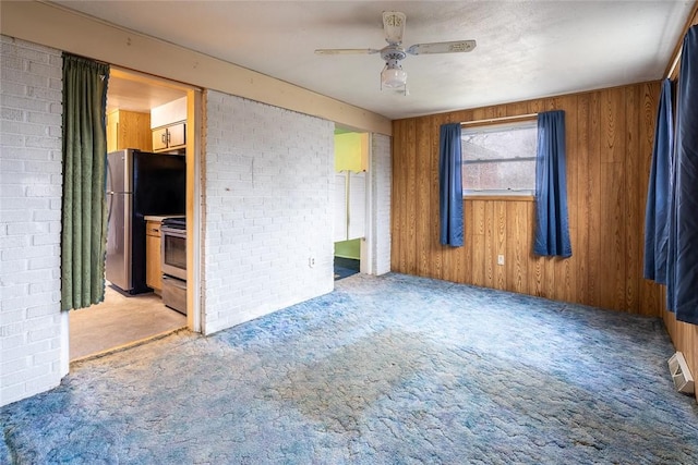 unfurnished room featuring ceiling fan, carpet flooring, and wood walls