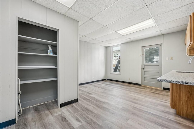 interior space with sink, a drop ceiling, light hardwood / wood-style flooring, and wooden walls