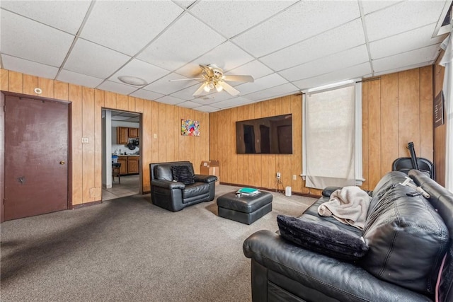 living room featuring ceiling fan, a drop ceiling, wood walls, and light carpet