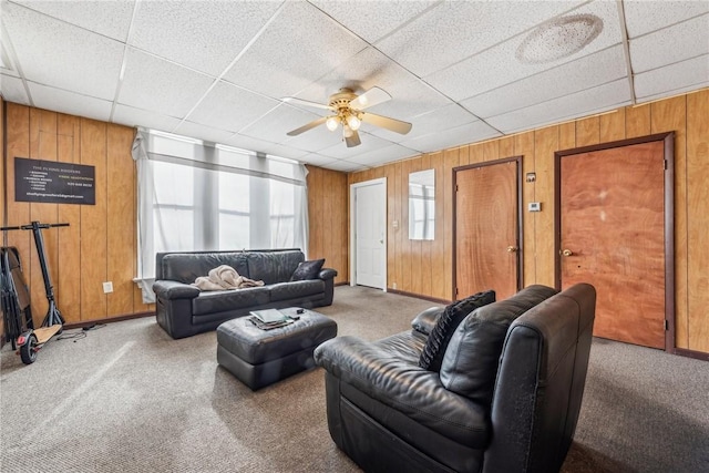 living room featuring carpet floors, a paneled ceiling, ceiling fan, and wooden walls