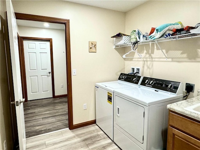 laundry room with light wood-type flooring, washing machine and clothes dryer, and cabinets