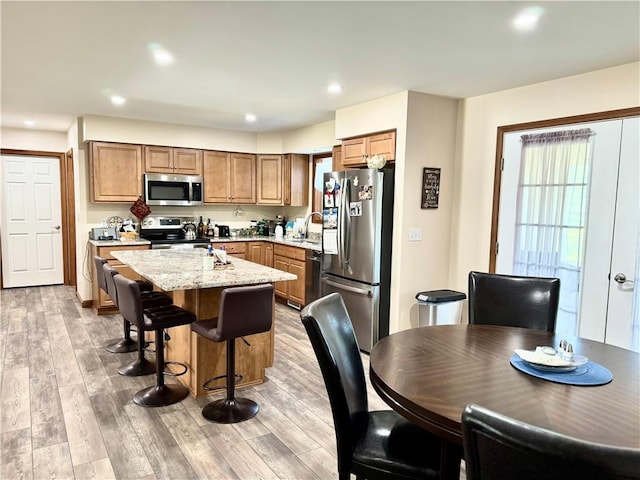 kitchen with light stone countertops, appliances with stainless steel finishes, a center island, a kitchen breakfast bar, and light hardwood / wood-style flooring