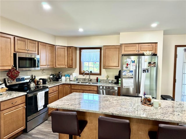 kitchen with sink, light hardwood / wood-style flooring, appliances with stainless steel finishes, a breakfast bar area, and light stone counters