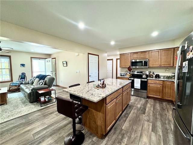 kitchen featuring ceiling fan, a kitchen island, dark wood-type flooring, a breakfast bar area, and stainless steel appliances