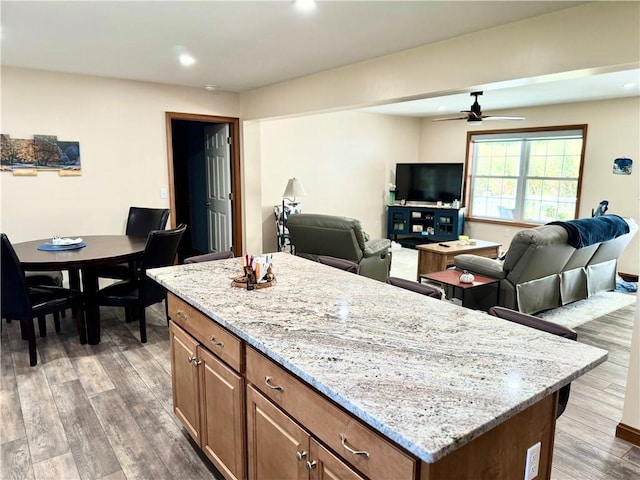 kitchen with ceiling fan, hardwood / wood-style floors, light stone counters, and a kitchen island