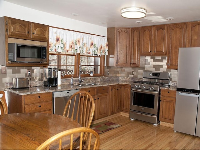 kitchen featuring light wood-type flooring, stainless steel appliances, light stone counters, and sink